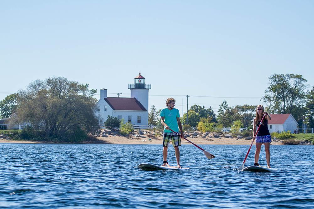 Two people paddleboarding past Sand Point Lighthouse in Escanaba.