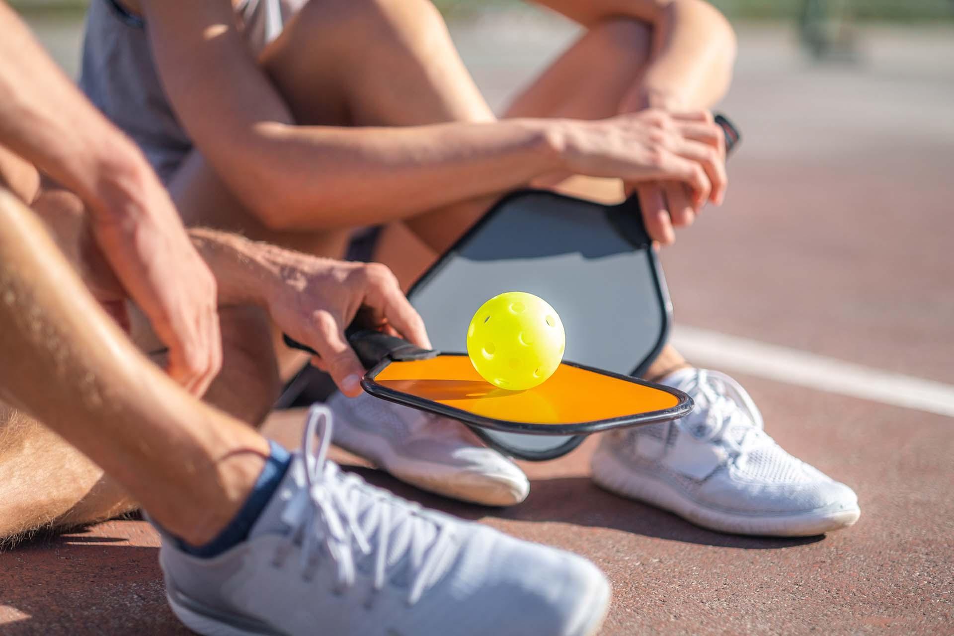 Two people sitting on a court holding paddles and a ball.