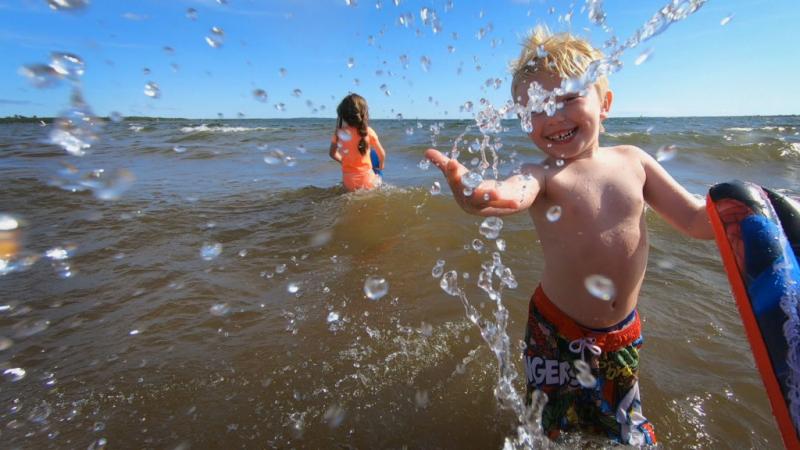 young boy at beach splashing water at camera